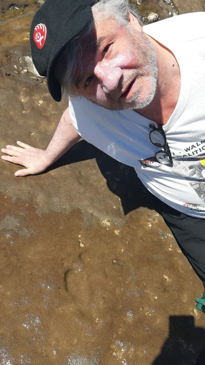 Huella fósil de megaterio en la playa de Pehuen Co, con una mano al lado para comparar el tamaño